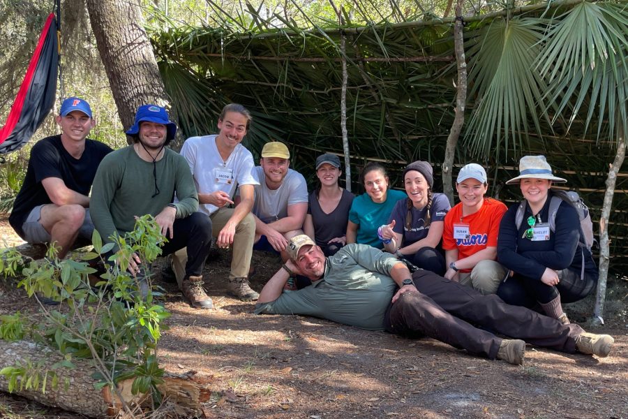 Students pose in front of a shelter made of palm leaves.