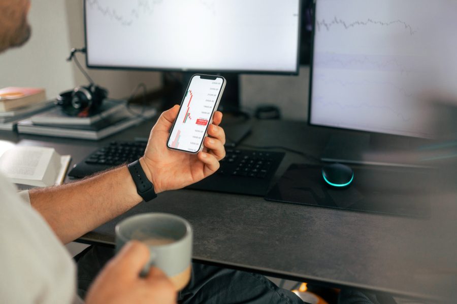 Man holding mobile phone with with investment graphics in one hand and a coffee cup in the other hand