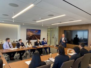 A group of students sit at a conference table while listening to Brad Smithy speak at the front of the room.