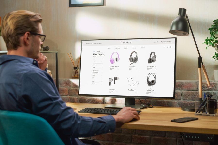 Over shoulder view of a man sitting at a computer in his home shopping for headphones