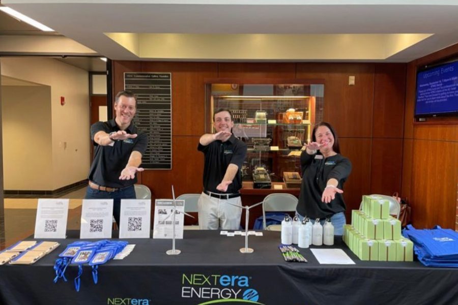 Three NextEra Energy representatives gator chomp at a recruiting table in Gerson Hall