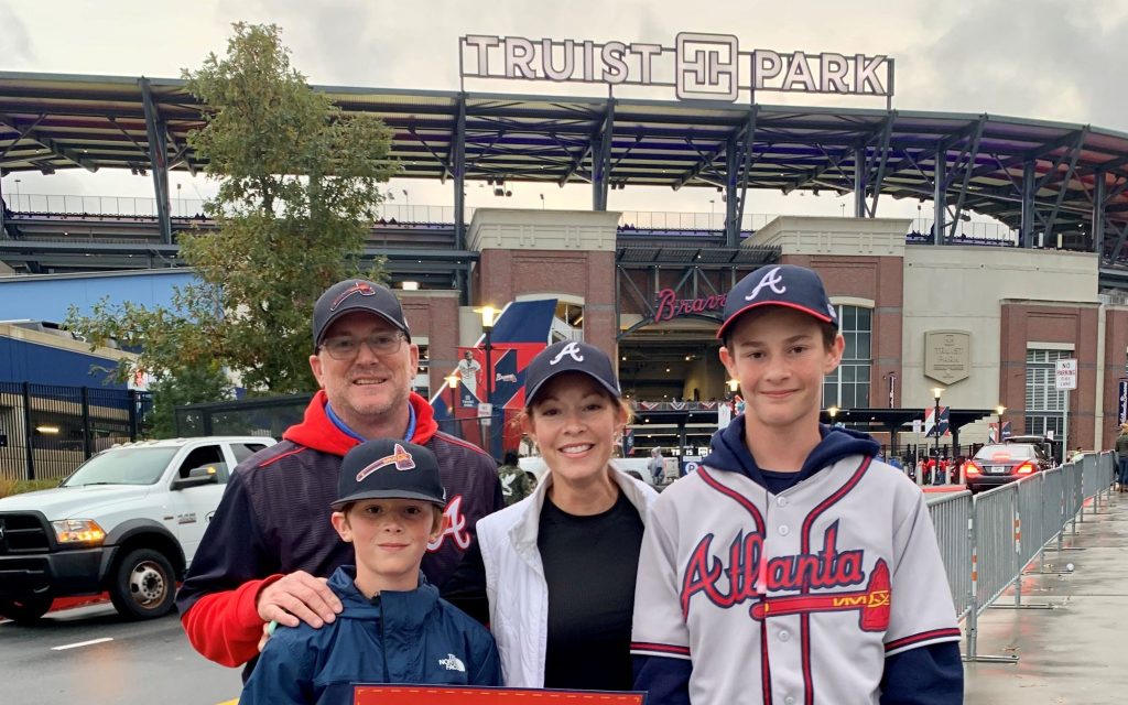 Katie Saez's family of 4 wearing Atlanta Braves attire pose for a photo in front of Truist Park.