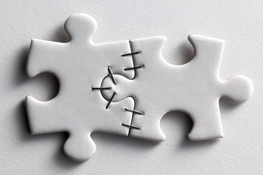Two white jigsaw puzzle pieces stapled together on a white background