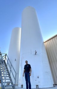 Matt McLean stands in front of equipment at an orange juice facility.