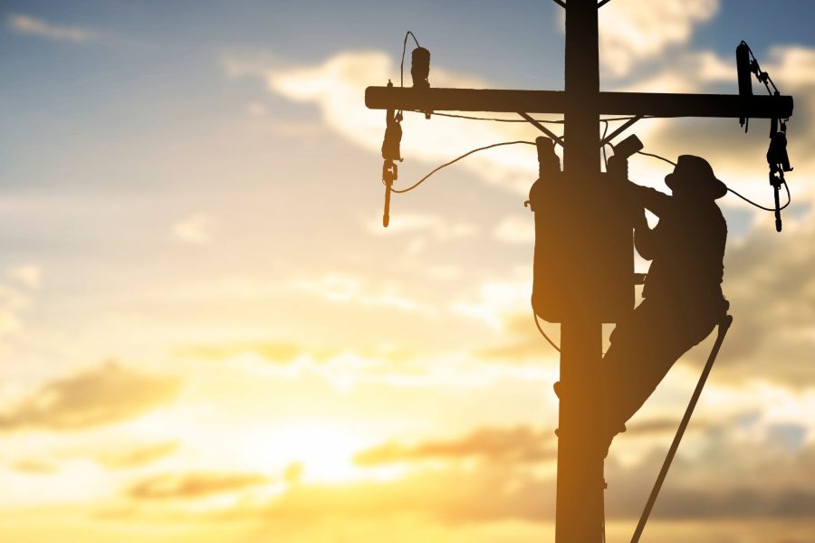 Silhouette of a linesman on a power pole working on a transformer