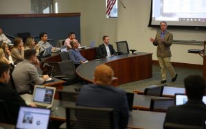 Rick Scarola speaks in front of a classroom of students.
