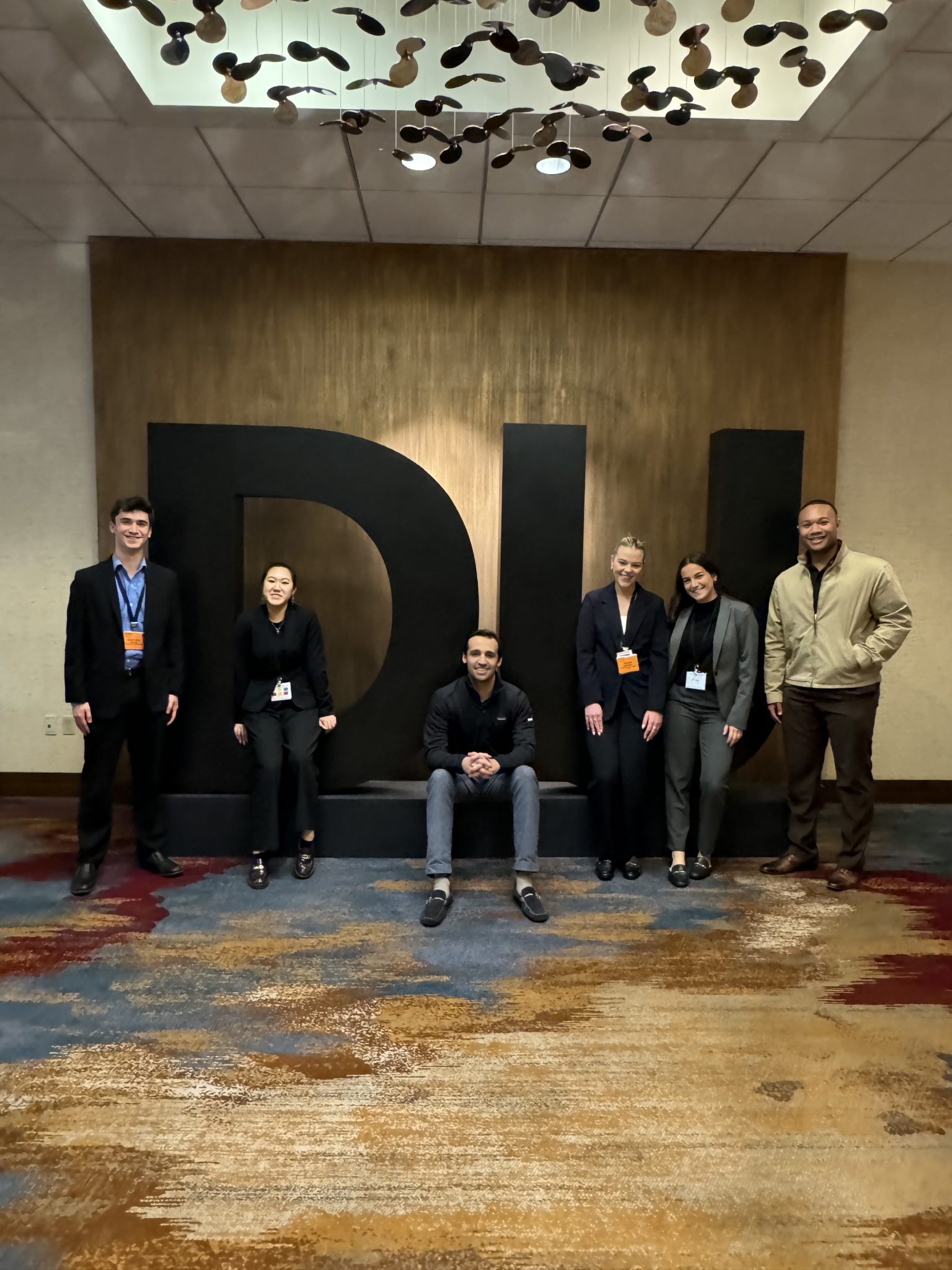 Students pose with their advisor in front of Deloitte University logo.
