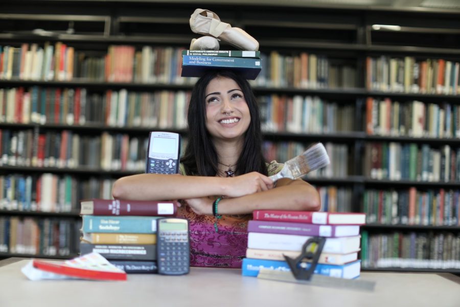 A student holds various objects while balancing books and ballet shoes on her head.