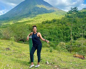 Lisa Thelwell poses for a photo in a lush green forest with a mountain in the background.