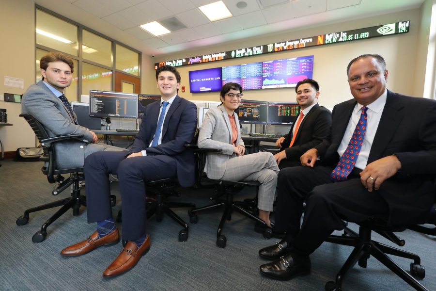 Four students and Eddie Sanchez sit in front of Bloomberg terminals.