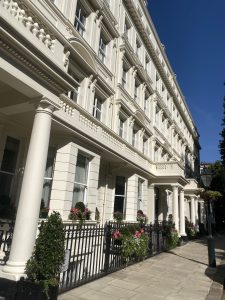 A white stone building with wrought iron fence and flowers along the sidewalk