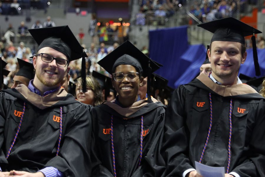 Three students wearing graduation regalia sit in a row during a graduation ceremony.