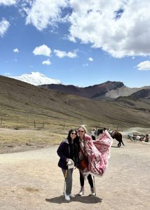 Two students pose in front of a mountain vista as someone behind them holds a saddled horse.