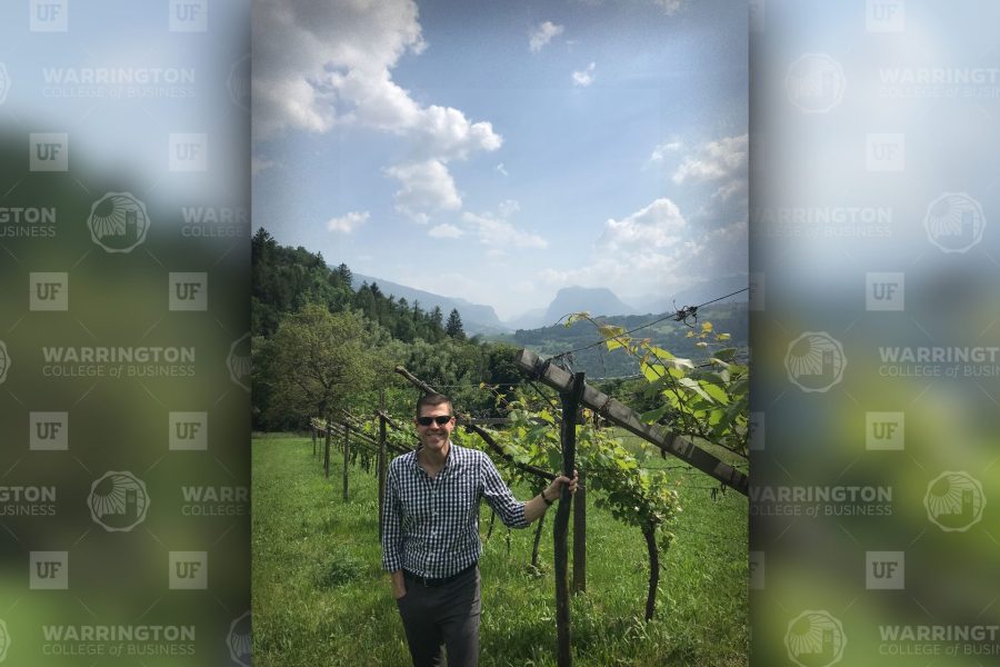 Rob Cornella stands in a lush vineyard surrounded by mountains.