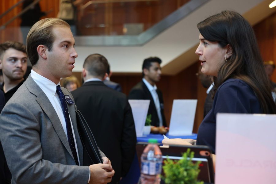 An MBA student wearing a suit speaks with another person in a suit at a networking event.