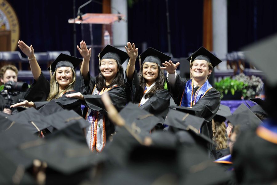 Four 2023-2024 Graduate students do the Gator Chomp wearing their cap and gown at the 2023-2024 Commencement Ceremony.