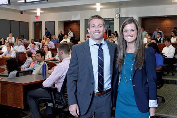 Michael and Sarah Peerson pose for a photo in a classroom full of students behind them. 