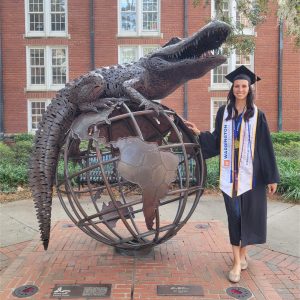 Rachael Kistner in graduation attire standing by the Gator Ubiquity Statue.