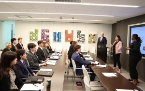 A group of students listen to a presentation by three UBS employees in professional attire.