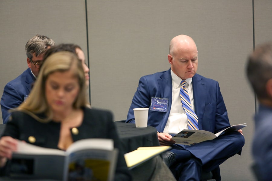 A judge in a navy suit attentively reviews a participant's financial plan during the Future Advisor Conference.