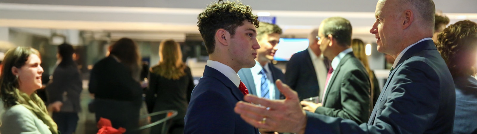 A student in professional attire listens attentively while networking with a financial advisor during the Future Advisor Conference.