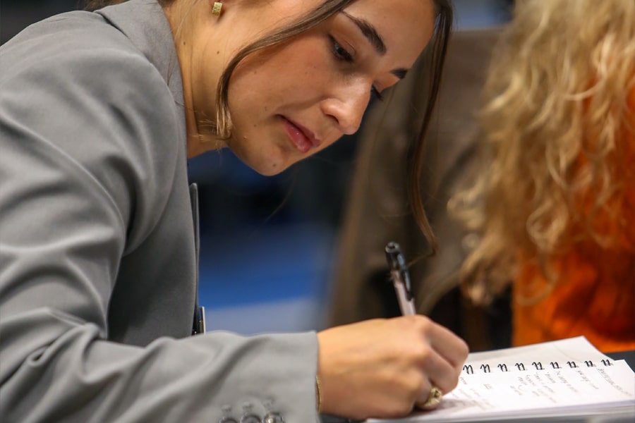 A student in business attire writes notes in a spiral notebook during a session at the Future Advisor Conference.