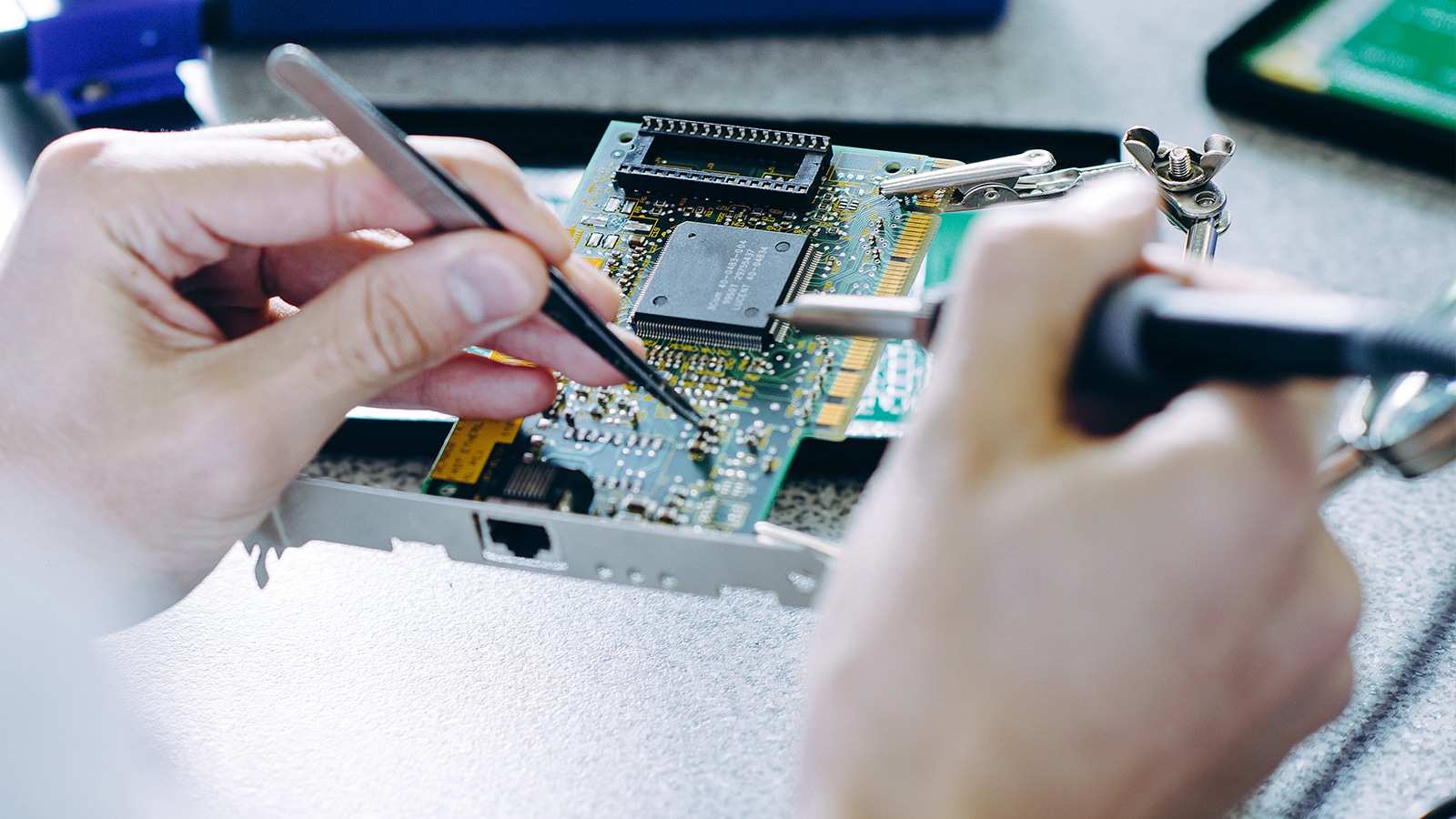 Close-up of a person using tweezers and a soldering tool to work on a computer circuit board, highlighting detailed microchip and hardware components.