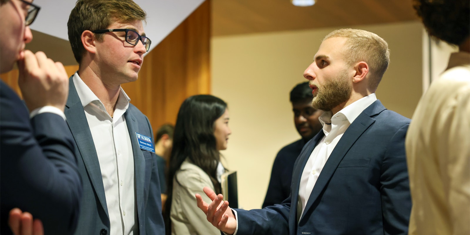 Two male students in business attire have a focused conversation during a GatorSLAM networking event.