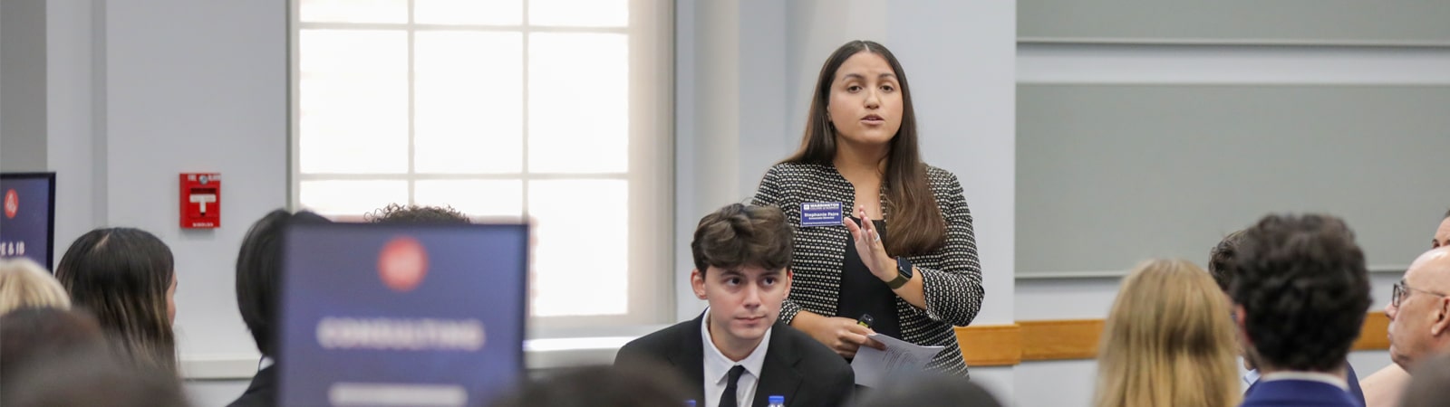 A student presents during a GatorSLAM mentorship activity while others attentively listen at tables labeled by industry sector.