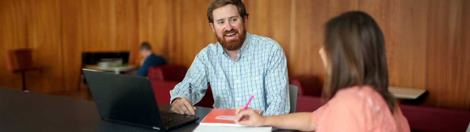 Graduate student consults with academic advisor while reviewing petition paperwork on a laptop.