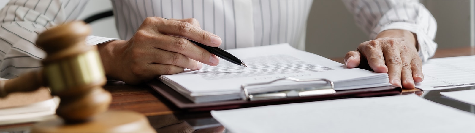 Close-up of a person reviewing a legal document with a pen, next to a wooden gavel on a desk—symbolizing legal scholarship and analysis.