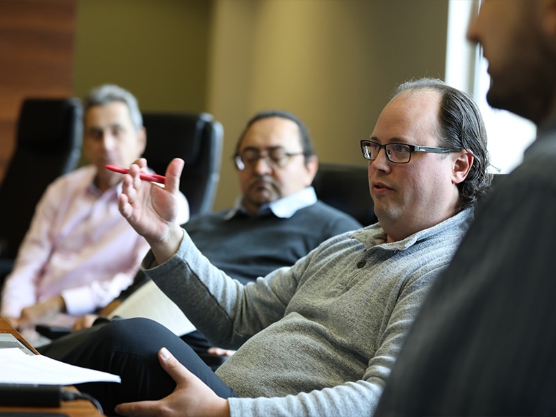 A group of legal scholars engaged in discussion around a conference table, with one participant speaking while others listen attentively.