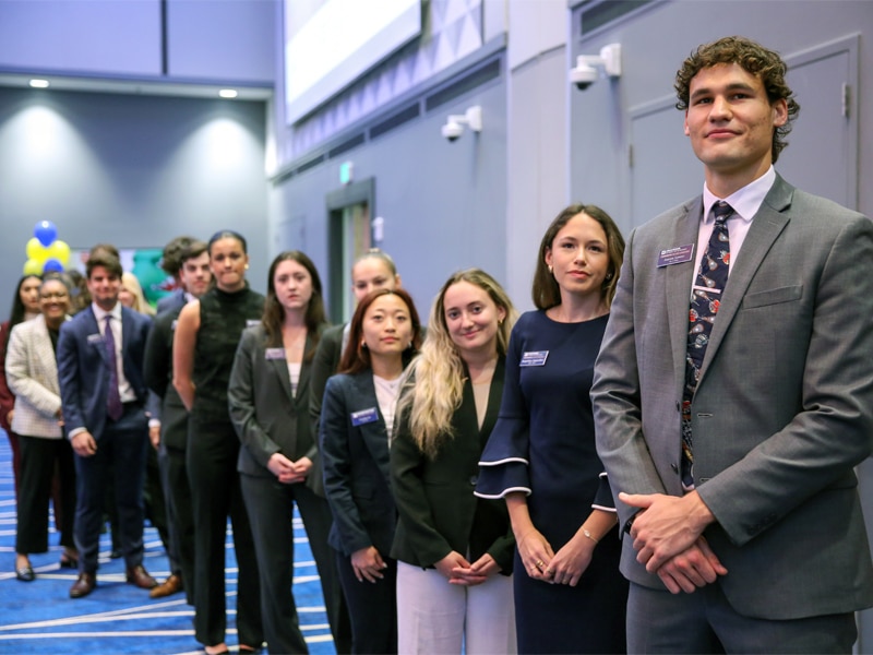 Students dressed in business attire stand in a professional line at a formal event, displaying poise and confidence.