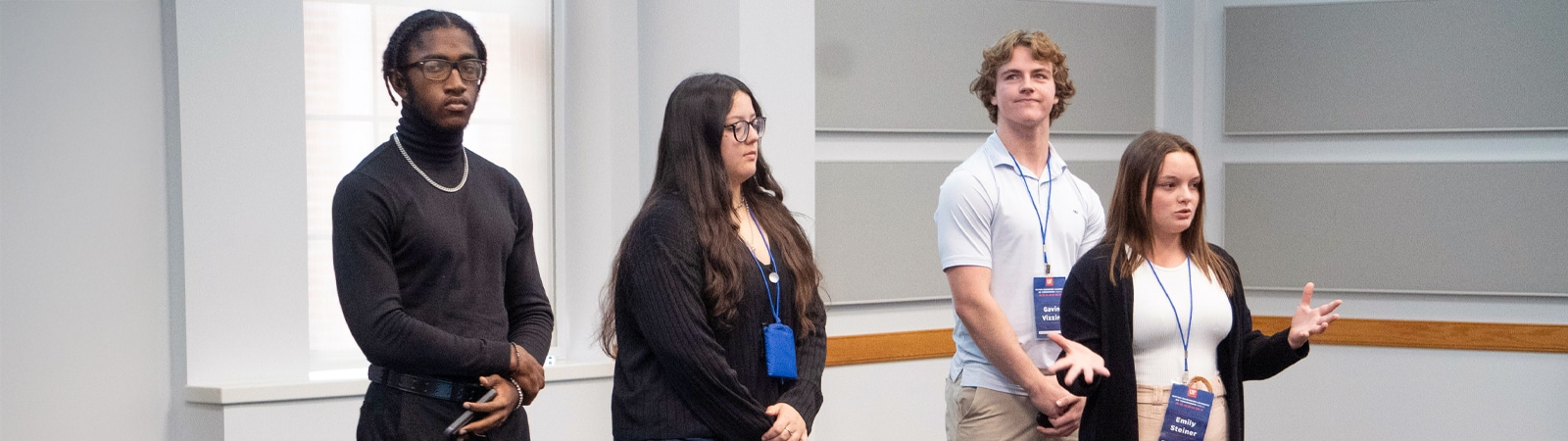 Four business students stand at the front of a classroom, presenting to their peers during a professional communication course.