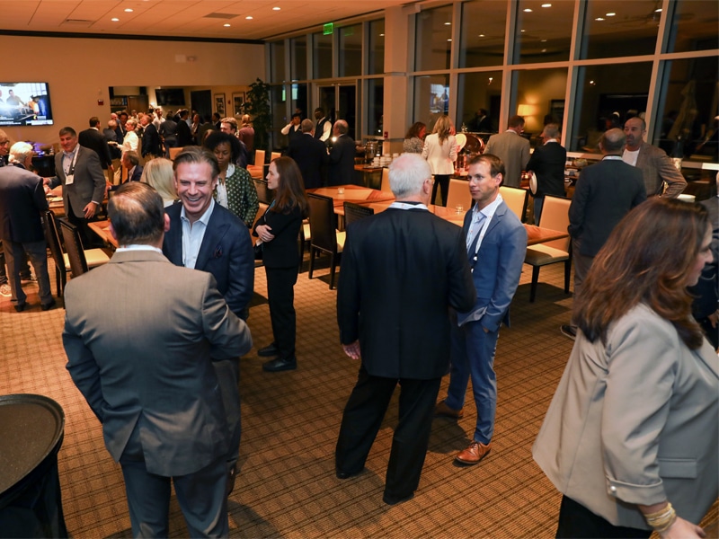 Attendees mingle during the ReConnect networking event, enjoying conversation in a warmly lit reception space with food and drinks.