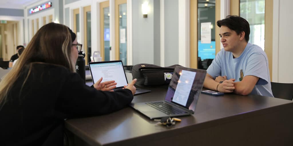 Two UF Warrington BS in Accounting students participating in the Volunteer Income Tax Assistance program have a discussion from behind laptops