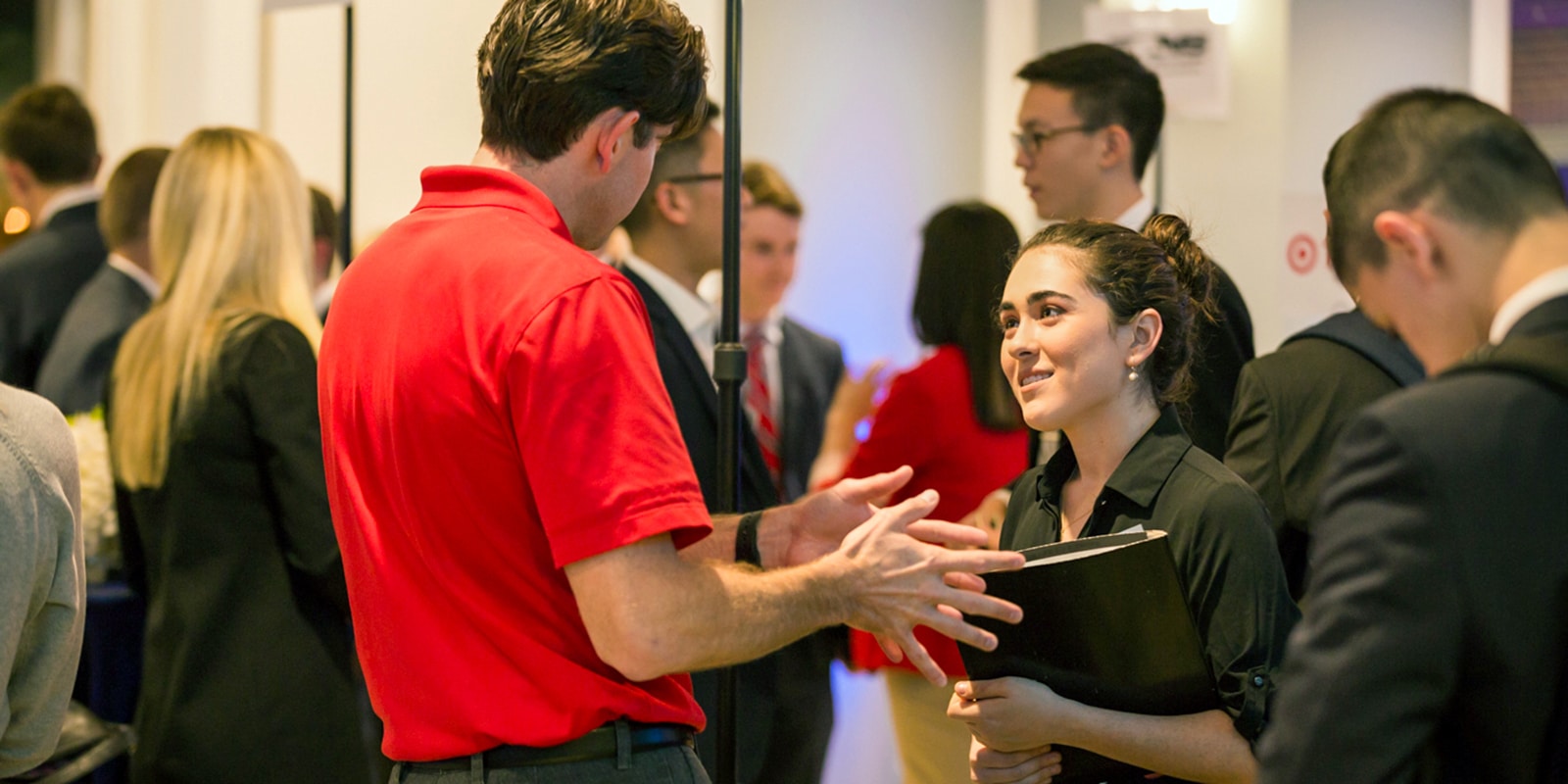Holding a folder, a student from UF Warrington's MS in ISOM - Data Science program listens to a recruiter talk about a job opening during a career fair