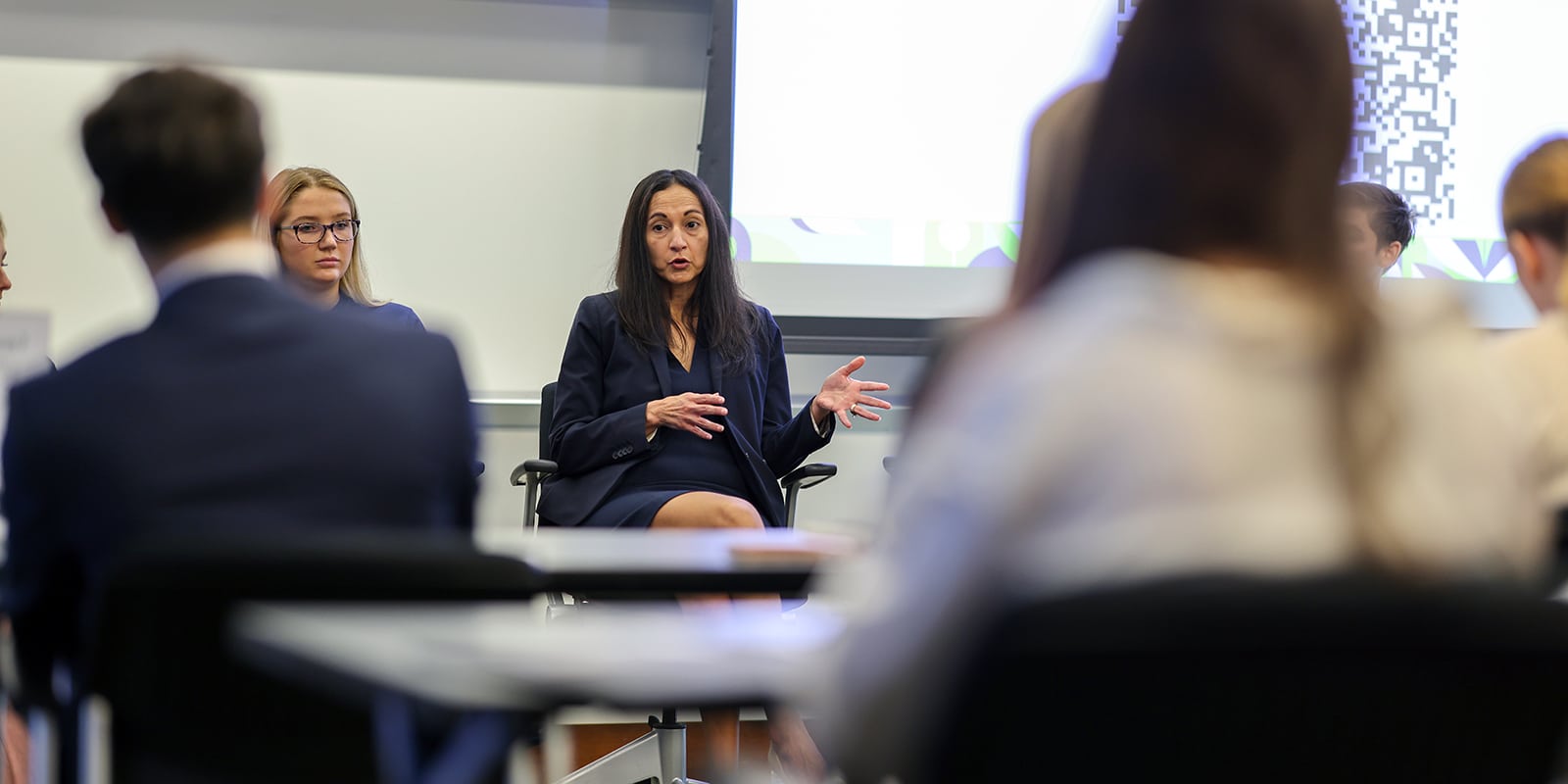 Sitting in a chair in front of a screen, a speaker talks about their company and career to a classroom of students from UF Warrington's MS in ISOM - Supply Chain Management program
