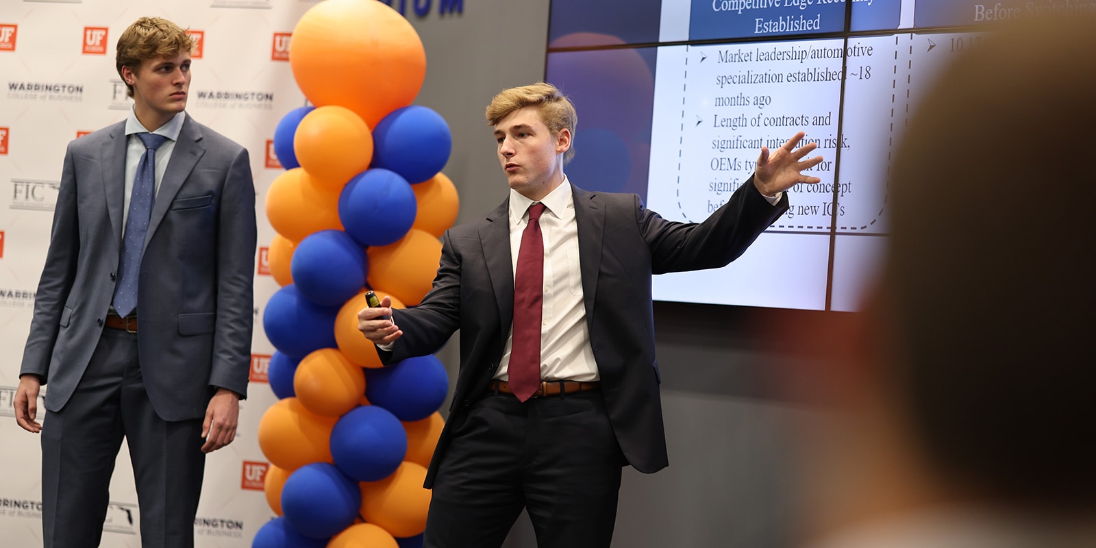 Two MS Marketing students from UF Warrington present on their marketing analytics project while standing near a column of blue and orange balloons