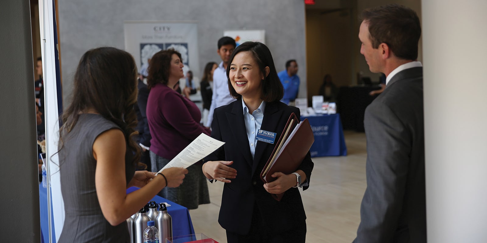 An MS Marketing student, holding a folder, smiles after handing her resume to a recruiter at a UF Warrington career fair