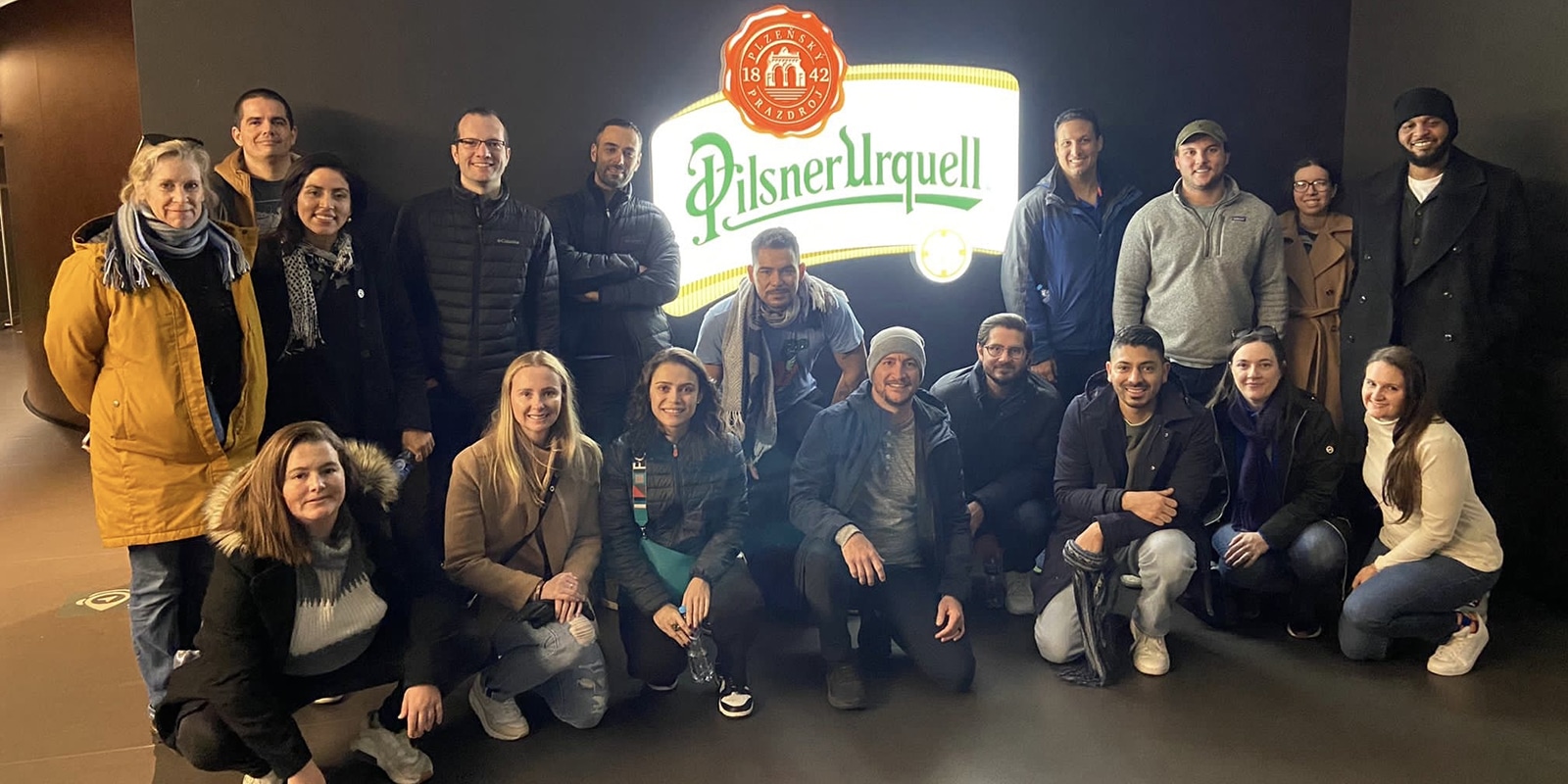 A group of MS Marketing students from UF Warrington pose in front of a lit Pilsner Urquell sign during their Global Immersion Experience