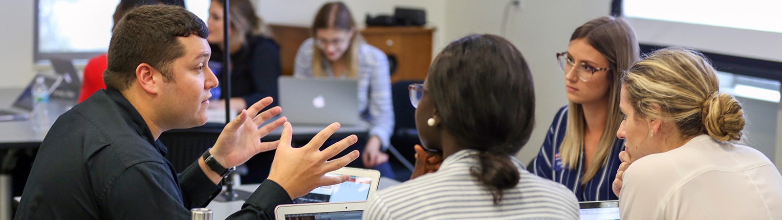 An instructor sits around a table with student from UF Warrington's Master of International Business program for an engaging discussion
