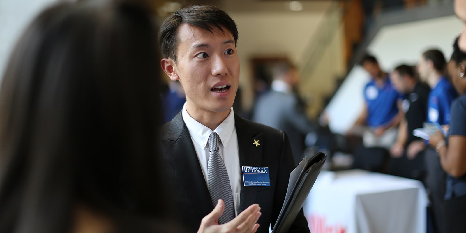A student in a nametag and suit from the University of Florida Warrington College of Business' Master of International Business program speaks with a recruiter during a career fair