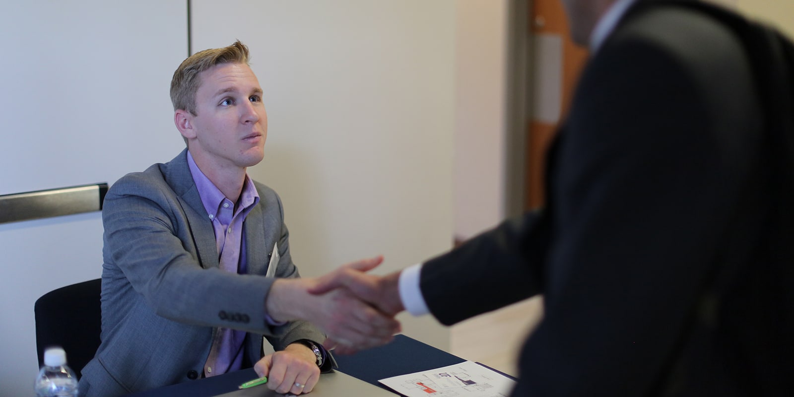 A student from UF Warrington's MSM program shakes hands with a recruiter, sitting behind a table, during a career fair