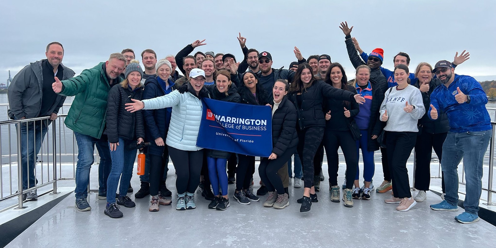 During a study abroad experience, students from UF Warrington's MSM program hold a sign and pose in a group for a photo by a railing
