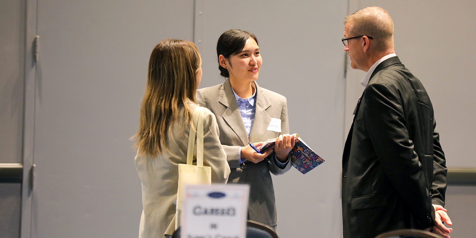 Two students from the University of Florida Warrington College of Business' Master of International Business program speak with a recruiter while taking notes at a career fair
