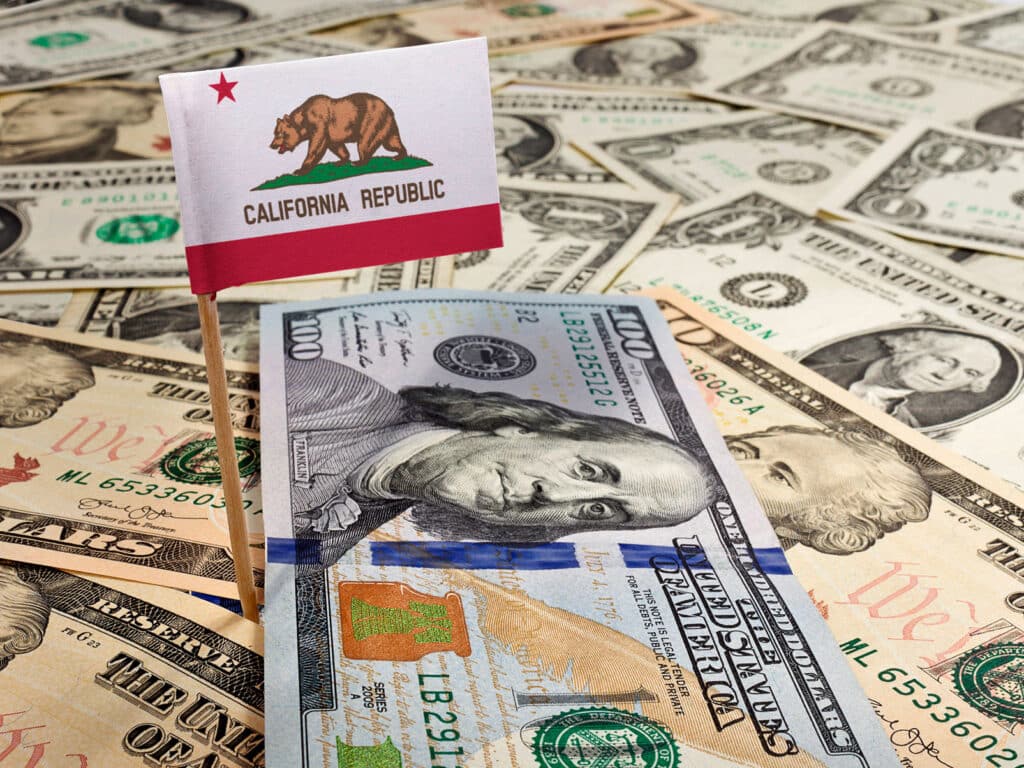 A small California flag with paper money of various amounts laying all around it