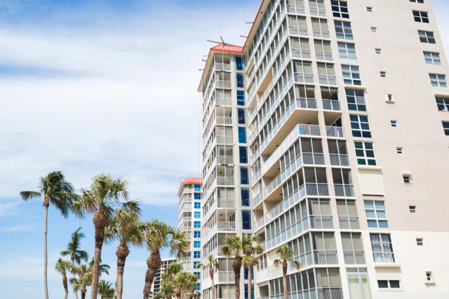 Tall condos with palm trees and wispy clouds on a blue sky