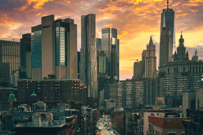 Looking down a street in New York City from a high vantage point with tall buildings and orange clouds in the background