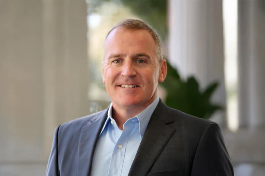 Albert Livingston, a man in a dark suit and light blue shirt, smiling with an architectural background of columns and greenery behind him.